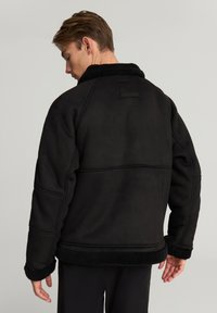 Giacca in pile nera con colletto, cuciture strutturate e tessuto testurizzato. Presenta un rivestimento morbido e soffice e una vestibilità leggermente oversize.