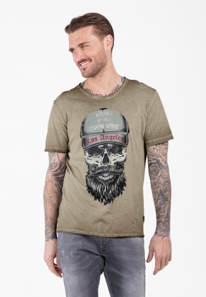 Camiseta verde oliva con cuello redondo, que presenta un gráfico de una calavera con una gorra que dice "Los Ángeles". Detalle de textura desgastada.