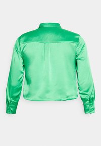 Camisa verde de satin com mangas longas e colarinho, textura suave e pregas nas costas para um detalhe adicional. Ajuste sob medida com punhos abotoados.