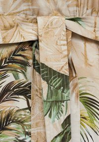 Tessuto leggero con un motivo a foglie tropicali in verde e beige. Presenta un design con cintura e una finitura testurizzata con cuciture sottili.