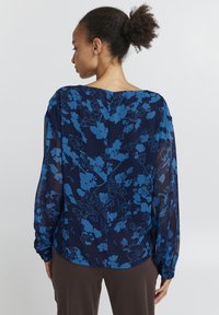 Blusa blu navy con tessuto trasparente caratterizzata da un motivo floreale blu, vestibilità morbida, maniche lunghe con polsini arricciati e scollatura ampia.
