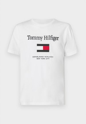 Balts kokvilnas T-krekls ar melnu izšuvumu "Tommy Hilfiger", zem tā ir krāsainā bloku logo (sarkans, zils, balts) un uzraksts "Established MCMLXXXV New York City."