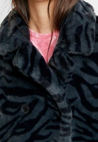 Manteau en fausse fourrure noire avec un motif à rayures de tigre, doté d'un col cranté et d'une fermeture à double boutonnage, texture douce et tissu moelleux.