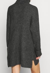 Mörkgrå ribbad stickad polotröja klänning med långa ärmar och sidslitsar, bärs av en person sedd bakifrån.