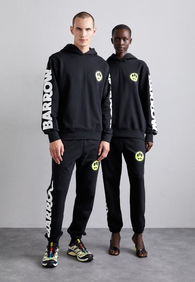 Svarte hettegensere og joggebukser har hvit "BARROW"-tekst på ermene og beina, med neongrønne smilefjes-logoer på fronten.