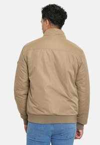 Chaqueta bomber color marrón claro con cuello alto, puños acanalados y cinturilla. Fabricada en un material ligero y suave. La vista trasera muestra su simplicidad.