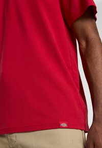 Camiseta de algodón roja con mangas cortas, escote redondo y una pequeña etiqueta de logo cerca del dobladillo. Textura suave, ajuste estándar.