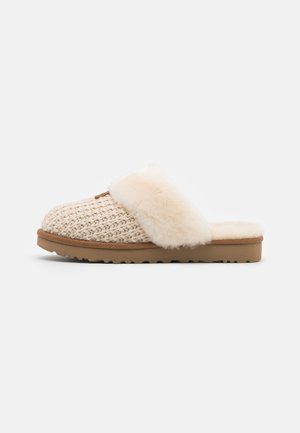 Beige knitted slip-on slipper with plush fur cuff and cushioned brown rubber sole, designed for indoor comfort.