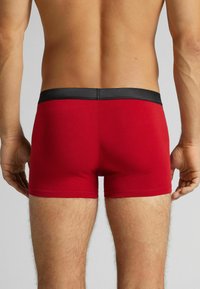 Bóxers de algodón rojo con una cintura negra, forma ajustada y textura suave, mostrando la vista trasera y detalles mínimos de costuras.