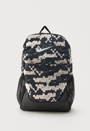 Rucsac Nike cu model camuflaj negru și alb, cu buzunar frontal mare, buzunare laterale din plasă și mâner superior, poziționat vertical pe un fundal simplu.