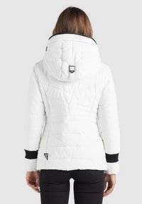 Doudoune blanche avec un design matelassé, capuche et accents noirs sur les poignets. Dispose d'un crochet pour un maintien sécurisé et d'une étiquette de logo à l'ourlet.