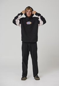 Felpa nera con maniche bianche a contrasto e logo grafico sul petto. Abbinata a pantaloni neri e scarpe con motivo mimetico.