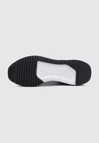 Svart gummisula på sneakers med texturerade spår, med en vit mellansula och präglad logotypdetalj. Platt profil, hållbar design.