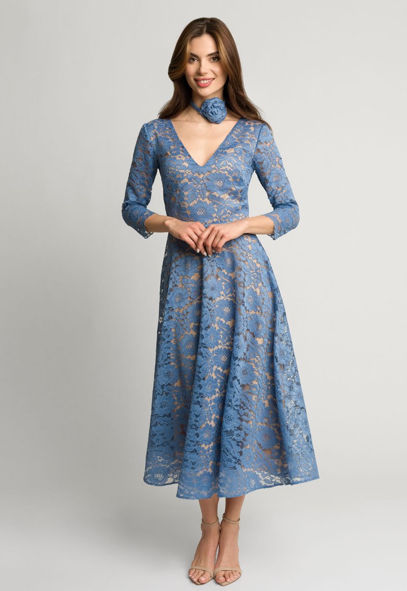 Niebieska sukienka w koronkę z rękawami 3/4, głębokim dekoltem w kształcie litery V oraz rozszerzaną spódnicą midi. Do kompletu dołączony jest pasujący, kwiatowy choker.