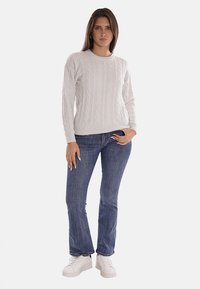 Maglione grigio chiaro a maglia con collo rotondo, abbinato a jeans blu a vita media e sneakers bianche. La texture è morbida e con un motivo.