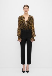 Langarm, doorschijnend blouse met ruffles in een bruine en groene bloempatron, gecombineerd met zwarte getailleerde broeken en zwartepuntige hakken.