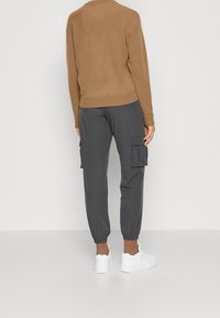 Brun fleece-tröja med rund halsringning, i kombination med mörkgrå joggerbyxor med sidofickor och elastiska manschetter. Vita sneakers.