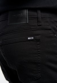 Jeans in denim neri con una patta di pelle etichettata "BIG STAR" sulla vita. Presentano cuciture a contrasto e una piccola etichetta intrecciata sulla tasca.