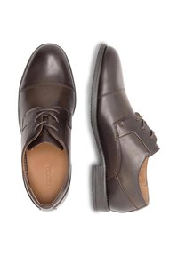 Brūni ādas kleita apavi ar aukliņu dizainu, gludu tekstūru, noapaļotu purngalu un kontrastējošu zoli. Iezīmējas ar smalku šuvju un iekšējo akcentu klātbūtni.