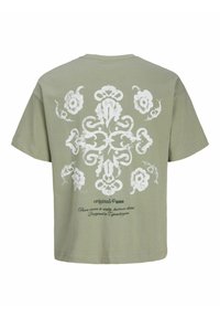 Λαδί πράσινο μπλουζάκι με λευκό λουλουδένιο και στολισμένο σχέδιο σταυρού στην πλάτη και μαύρο καλλιγραφικό κείμενο «Από το όραμα στην πραγματικότητα, περιοχή Χόλμεν.»