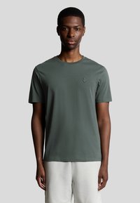 Korte mouwen donker groene katoenen t-shirt met een ronde hals, voorzien van een klein geborduurd logo op de linkerborst. Soepele textuur.