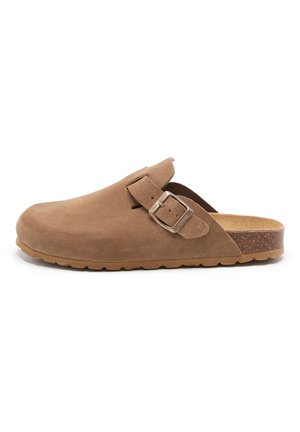 Sabot en suède marron avec une semelle plate, détail de boucle sur le côté et un revêtement de pied texturé. Dispose d'un orteil arrondi et d'un design minimaliste.