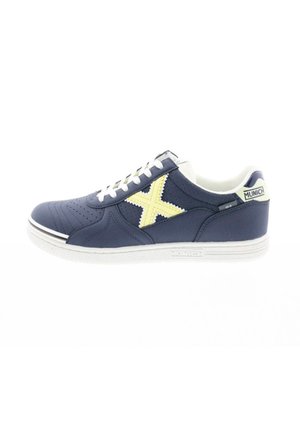 Zapatilla deportiva azul marino con detalles perforados, suela blanca, logo amarillo en forma de "X" y cordones blancos. Parte superior de tela texturizada.