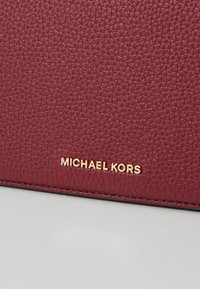 Bordeaux lederen portefeuille met een reliëf-gouden "MICHAEL KORS" logo. Heeft een gladde, glanzende afwerking.