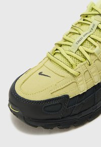 Sapatilha Nike com parte superior em camurça e rede amarelas, sola de borracha preta e atacadores tonais com um pequeno logótipo de lado.