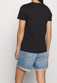 Černé tričko s krátkým rukávem vyrobené z bavlny, spárované se světle modrými džínovými šortkami. Šortky mají ohrnuté manžety a dvě zadní kapsy.