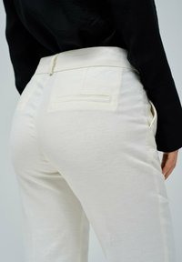 Pantalones de lino blanco con mezcla, con bolsillos laterales y traseros, corte ajustado y una textura suave. La cinturilla presenta un lazo central.