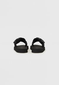 Sandales noires avec une semelle plate, des sangles réglables et un design simple et moderne. Fabriquées à partir de matériaux durables avec une finition texturée.