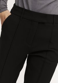 Schwarze, maßgeschneiderte Hosen mit glatter Oberfläche, featuring eine flache Vorderseite und seitliche Taschen. Der Bund sitzt auf Taillenhöhe.