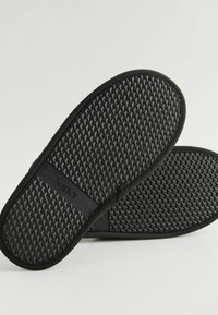 Tongs en caoutchouc noir avec une semelle texturée et un motif en losanges surélevé. Marquées "NEXT" sur la lanière, présentant une finition lisse dans l'ensemble.