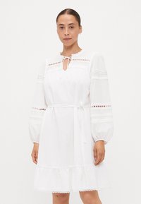 Vestido de algodão branco com barra franzida, mangas longas balão, detalhes em renda e um laço no pescoço. Possui padrões de ilhó nas mangas.