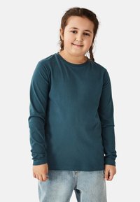 Long-sleeve, teal cotton t-shirt with a round neckline and soft texture, paired with light blue denim jeans.
