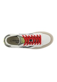 Zapatilla deportiva blanca con cordones rojos, detalles verdes y elementos de diseño negros. Presenta una puntera perforada y una suela de goma color marrón claro.