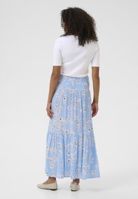 Jupe maxi bleu clair à motif floral avec une taille smockée et un design en couches. Une paire de ballerines beiges complète le look.