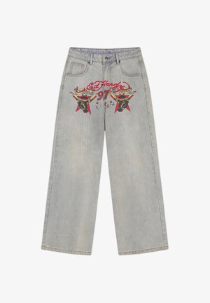 Hellgraue Jeans mit weitem Bein und Fronttaschen, versehen mit rotem "Ed Hardy 97"-Schriftzug und illustrierten Stierköpfen mit gelben Hörnern und Sternen.