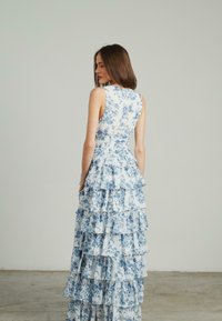 Vestido floral con patrones en azul y blanco, diseño sin mangas y falda de capas con volantes. Hecho de una tela ligera con un cuerpo ajustado.