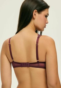 Biustonosz w głębokim burgundowym kolorze z koronkowymi akcentami, regulowanymi ramiączkami i zapięciem na hak. Gładka tekstura z półprzezroczystą tylną częścią.
