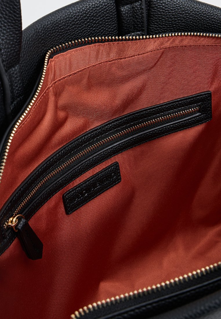 Intérieur d'un sac à main en cuir noir avec doublure en satin orange, comprenant une poche zippée noire et une étiquette texturée noire. Détails en zipper doré.