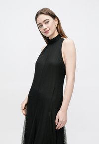 Black halter-neck dress with a textured fabric, flared silhouette, and subtle sheer detailing at the hem. Clean lines and smooth finish.