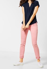 Marineblauwe blouse met korte mouwen en een V-hals, gecombineerd met lichtroze slim-fit jeans, opgerold bij de manchetten, en witte sneakers.