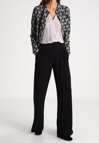 Black wide-leg trousers paired with a light-colored blouse and a patterned, fitted jacket featuring a floral design and no visible buttons.