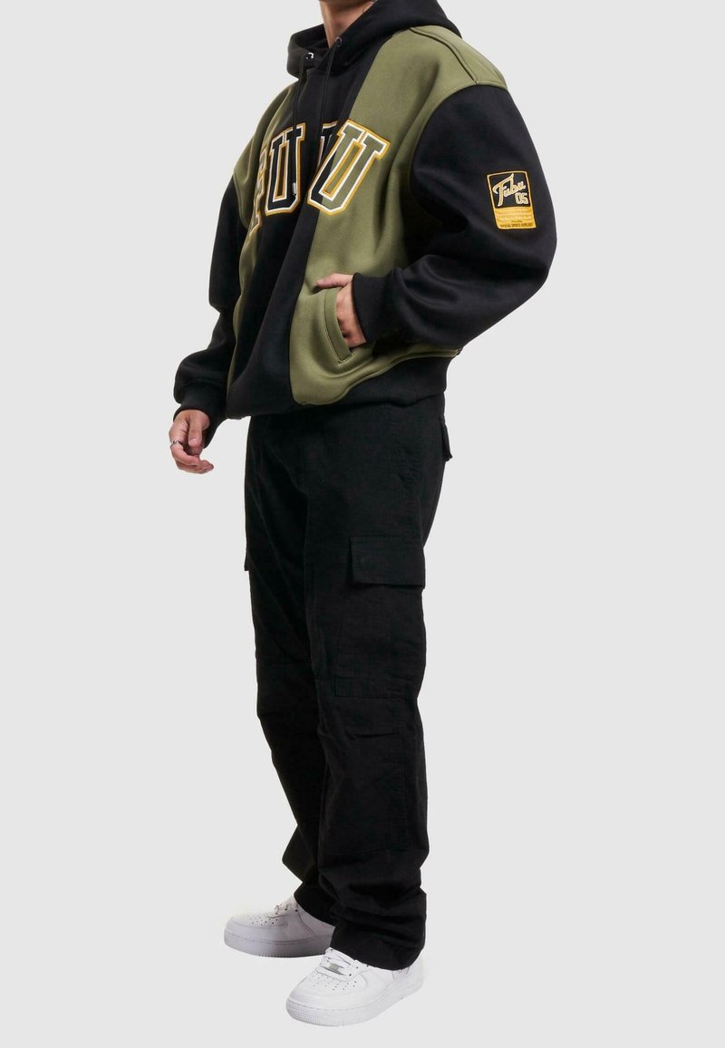 Huvtröja i svart och olivgrönt med stor text "PUU", sidfickor och en märkesdetalj på ärmen; kombinerad med svarta cargobyxor.
