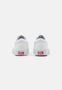 White Vans shoes featuring a smooth leather upper with embossed text, flat white laces, and a red logo on the heel. Low-top design.