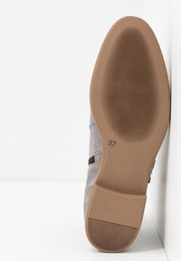 Harmaat kengät, joissa on teksturoitu pinta, mustat yksityiskohdat ja ruskea kumipohja, jossa on vaakasuorat urat. Koon merkintä 37 pohjassa.