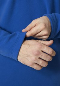 Niebieski polarowy ubiór z długimi rękawami. Zbliżenie na ręce regulujące mankiet, ukazujące miękką fakturę i detale stębnowania.