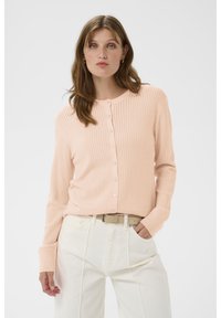 Hellrosa gerippte Strickjacke mit Knopfleiste, langen Ärmeln und rundem Ausschnitt, kombiniert mit weißen, hoch taillierten Hosen.